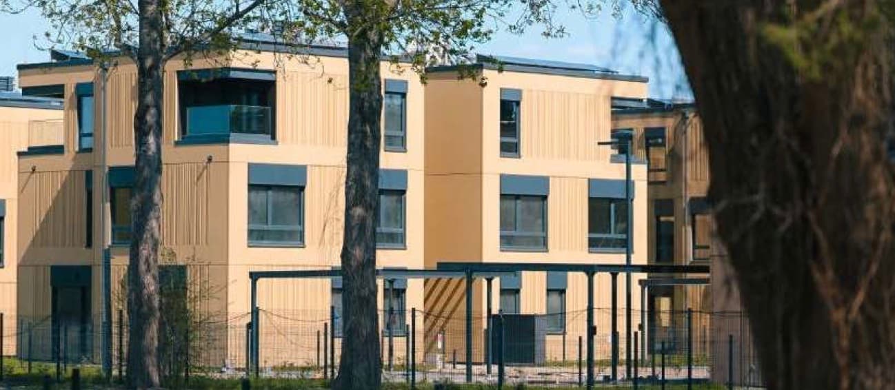 Wola Village, Krakau — fertiggestellte Modulgebäude mit Holzfassade zwischen Bäumen